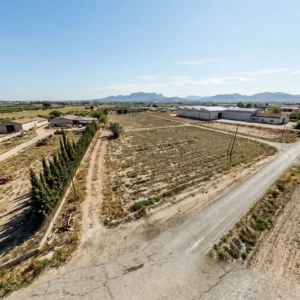 Parcela de terreno rústico junto a caminos y naves, con montañas al fondo en Marchena