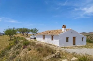 Casa rural blanca con tejado de teja entre árboles y paisaje árido