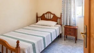 Dormitorio con cama de madera, mesita auxiliar y ventana en una vivienda de La Viña, Lorca