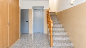 Portal interior con ascensor y escalera de terrazo en una vivienda de La Viña, Lorca