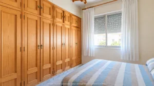 Dormitorio con armarios empotrados de madera, cama y ventana con persiana