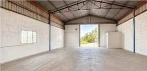 Interior diáfano de nave con suelo de hormigón, ventanas y gran portón abierto