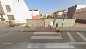 Solar urbano vallado entre viviendas, junto a una acera y un paso de peatones en Lorca