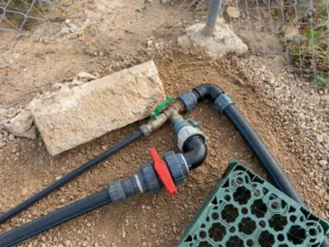 Tuberías negras y válvula roja de riego junto a una valla metálica en la parcela